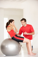Image of a personal trainer guiding a client to do exercises on a gym ball.